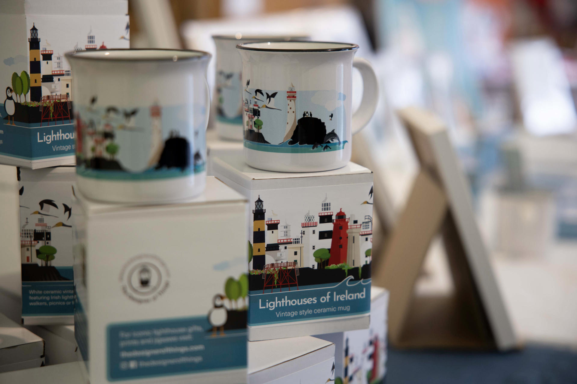 Mugs with lighthouse designs on a shelf with packaging labeled 'Lighthouses of Ireland'.