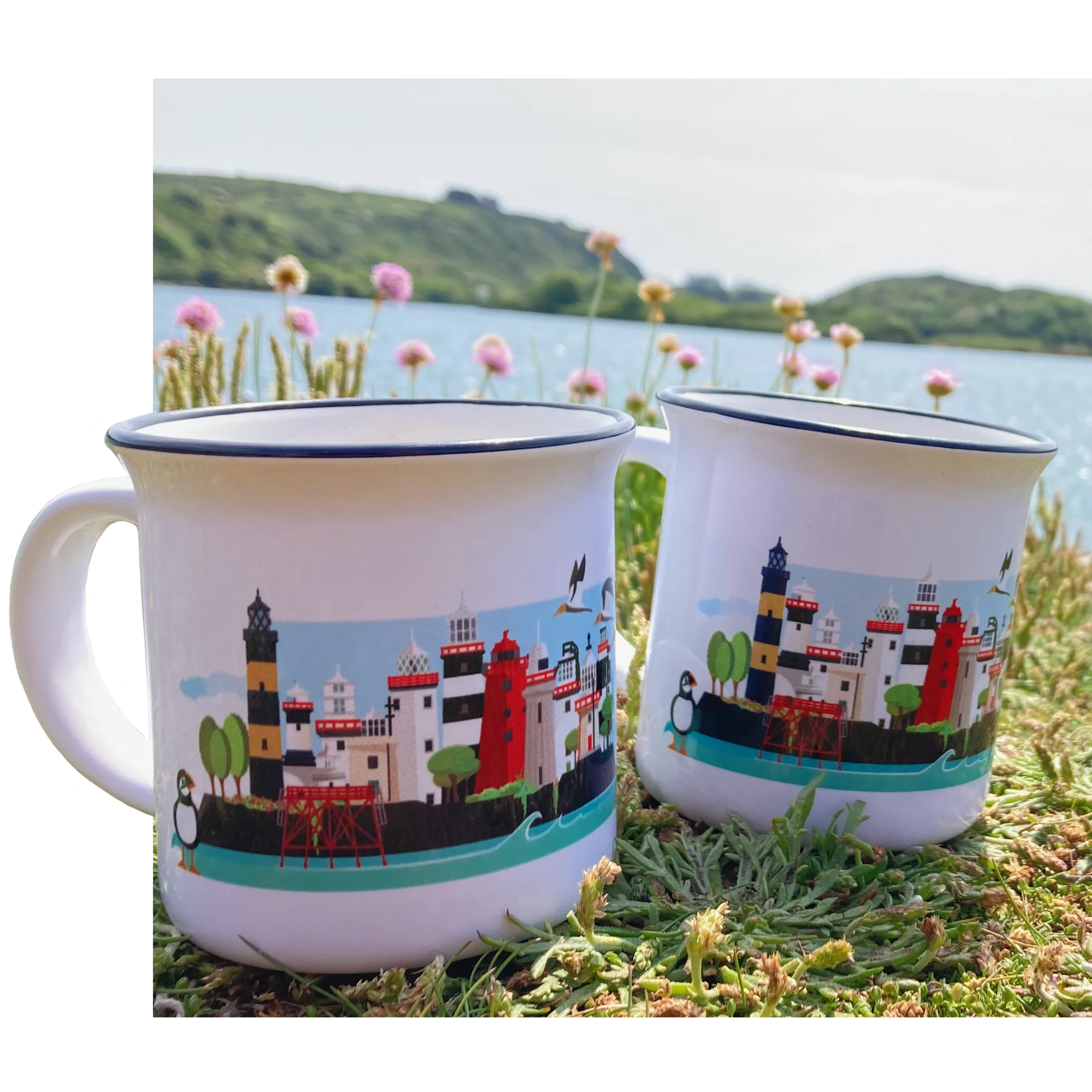 Two mugs with a scenic design of buildings and nature on grass with a lake in the background
