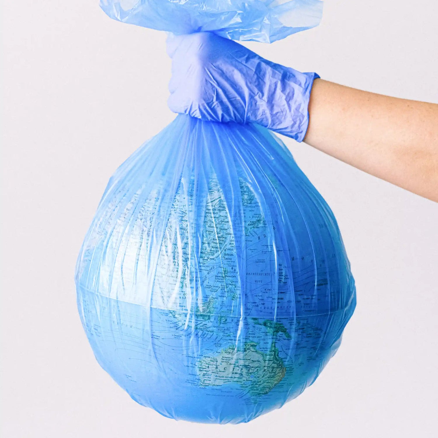 Globe wrapped in plastic bin bag held up by hand in glove